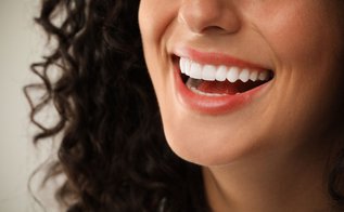 Smiling woman with healthy white teeth on a light grey background representing cosmetic dentistry services in Vaughan