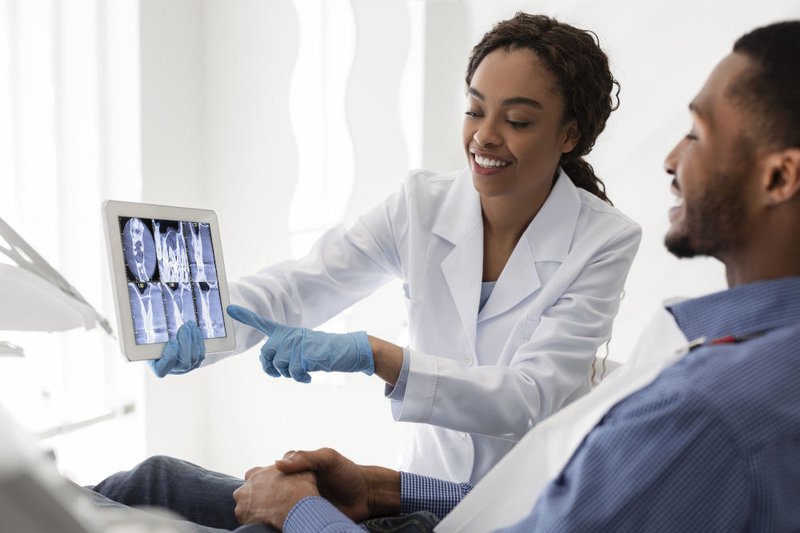 Smiling female dentist discussing treatment options such as root canal, extraction, or alternative procedures with a patient in a clinic.